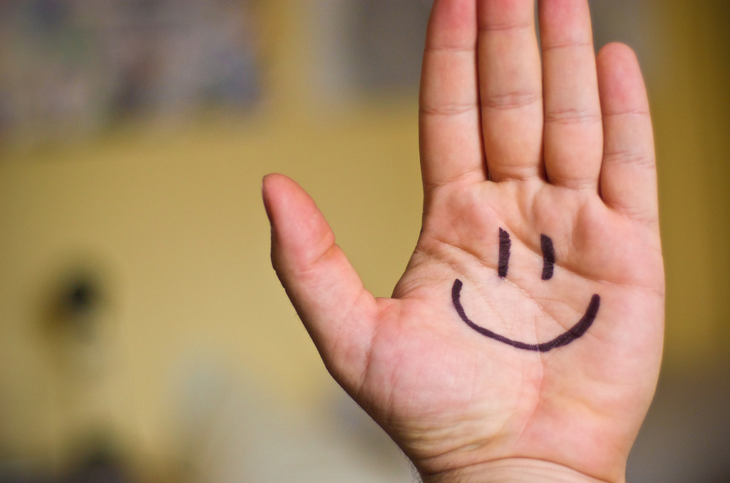 Smiley face drawn on a hand reminds us to be happy