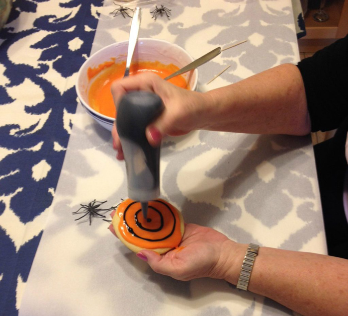 Adding spider web design on a sugar cookie with black icing