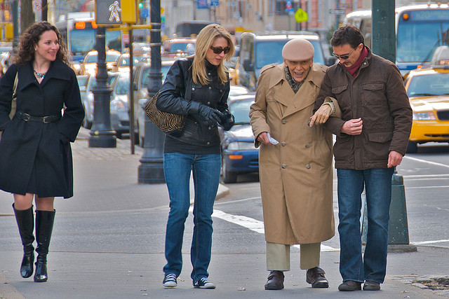 Adults assisting an elderly man across a street