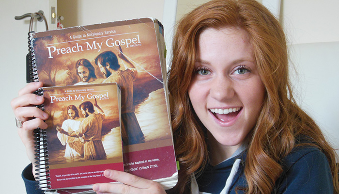 Young adult woman holding well used Preach My Gospel Missionary manuals