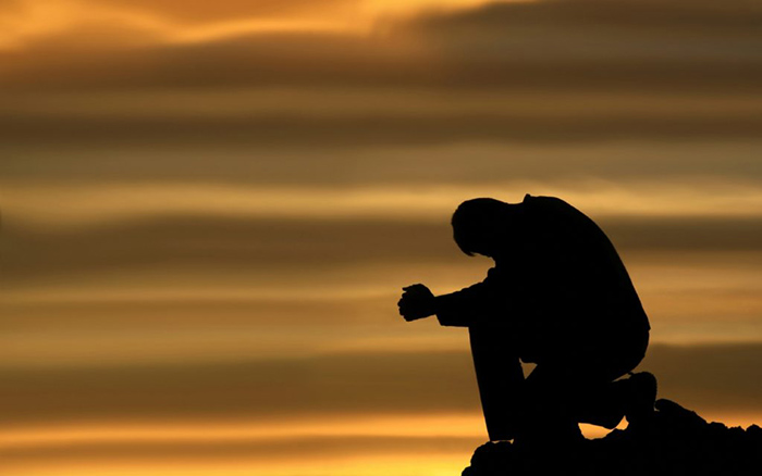 A man kneels on a mountain and prays