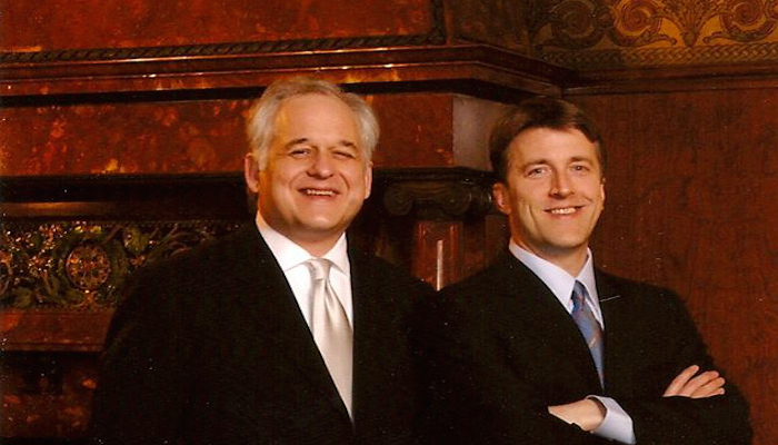 Two men standing side by side smiling.