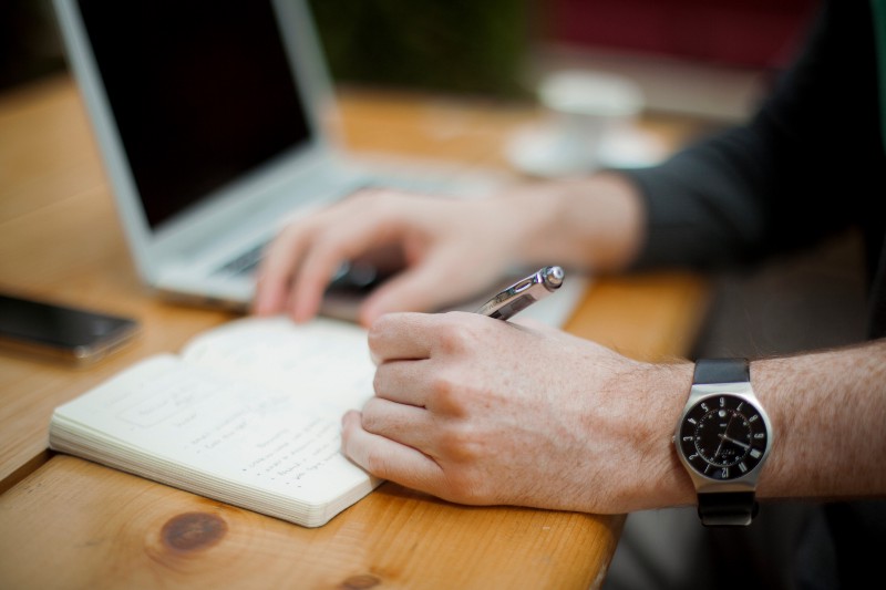 person using a computer and taking notes on a notepad