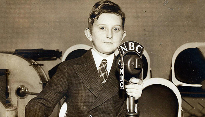 A child dresses up as a 1940s style announcer