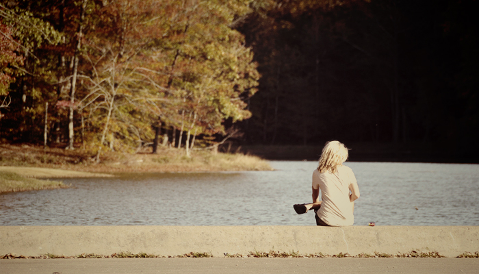 Woman sitting alone on a dock by a lake.