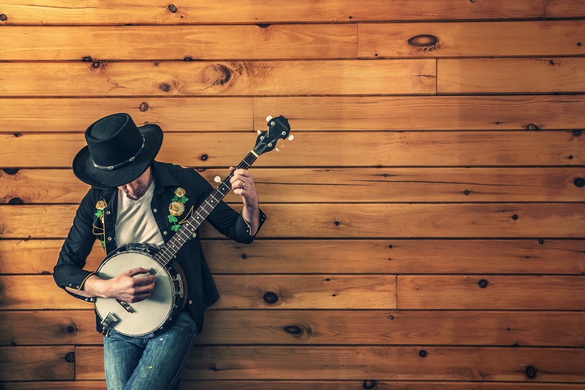 Man playing the banjo against a wood wall