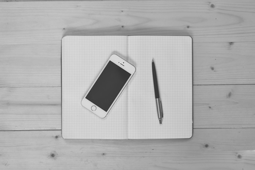 Black and White photograph of a notebook, phone, and pen on a table