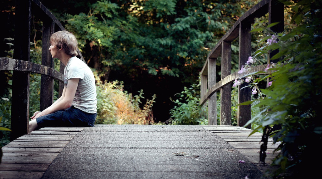 Teen Boy Listens to Music on a Bridge