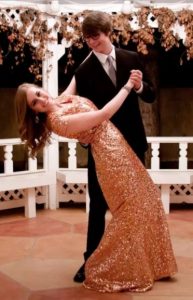 A boy dips a girl in a glittery prom dress.