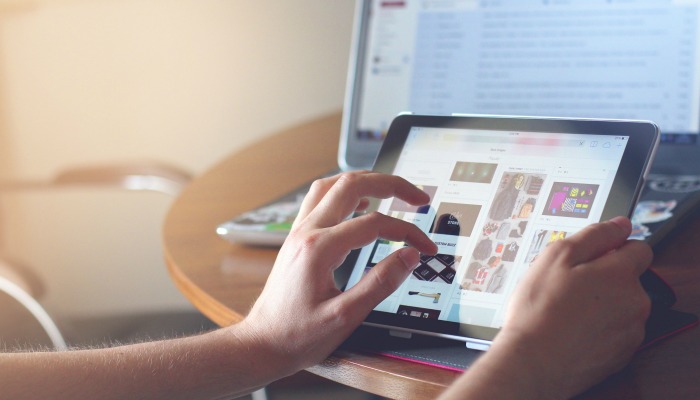 A person views social media on their tablet while their email is open on a laptop in the background.