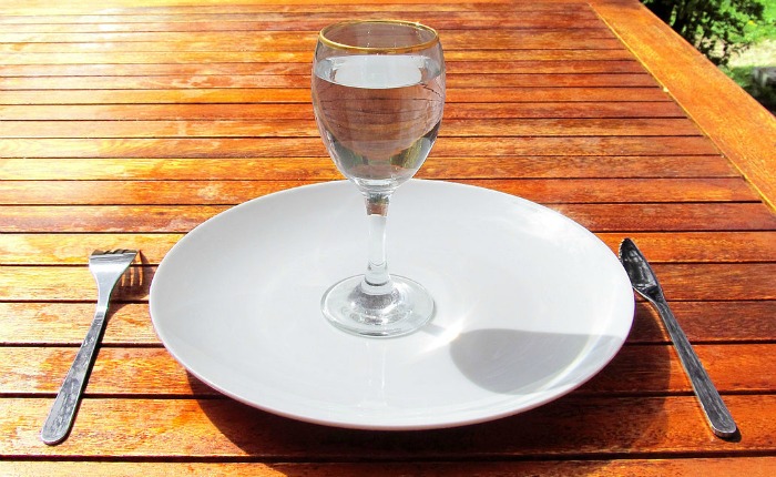 Glass of water on empty plate with fork and knife on table