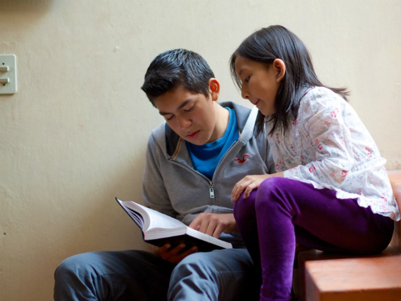 A brother and sister read the scriptures on some stairs.