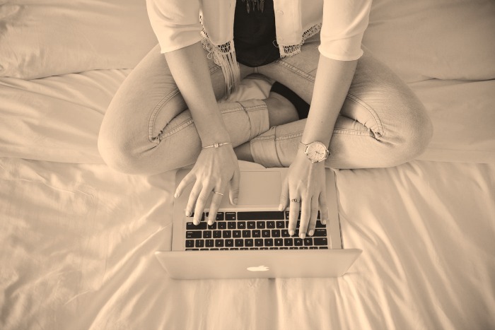 A woman types on a laptop in bed