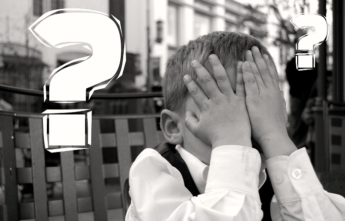 Boy Covering his face with question marks in the air behind him