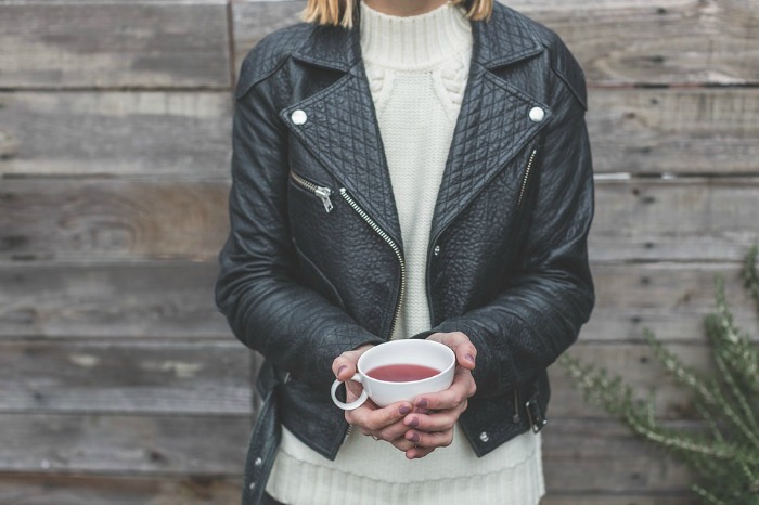 A Leather Jacketed Woman Holding tea in Front of wooden wall