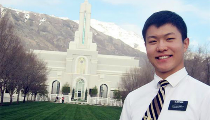 An LDS missionary of Asian decent is seen posing in front of an LDS temple with mountains in the background