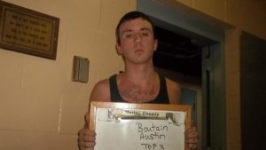 Austin Boutain is seen holding a white board with his name on it and is standing in front of a plain brick wall