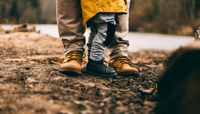 A close up shot of the feet of an adult and a child on the shores of a river