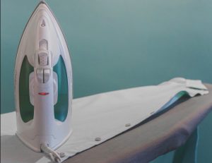 An Iron sits right side up on top of an ironing board that has a man's white dress shirt laying on it