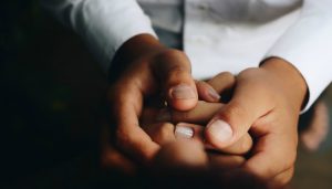 Large, dark brown hands hold smaller and similar hands