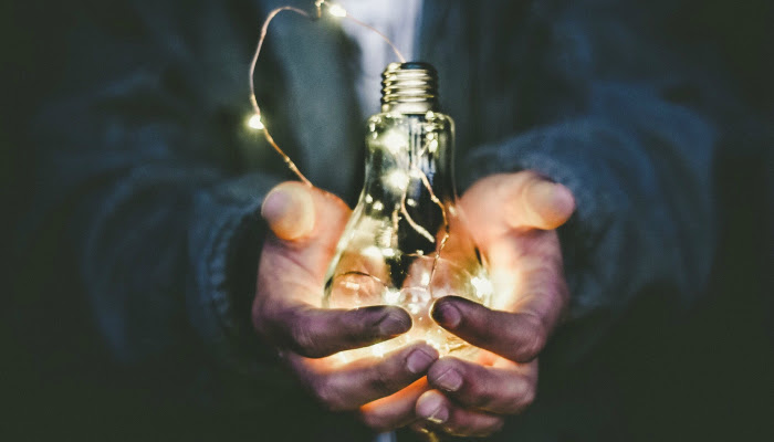 A man (that's only visible from the shoulders down) is seen holding a light bulb that has a string of lights lit up that are strung around and inside the light bulb