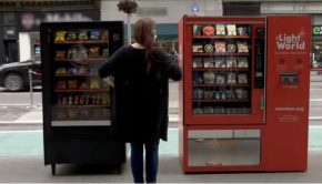 A woman stands between two vending machines, one black and on red, and appears to be attempting to choose between them