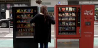 A woman stands between two vending machines, one black and on red, and appears to be attempting to choose between them