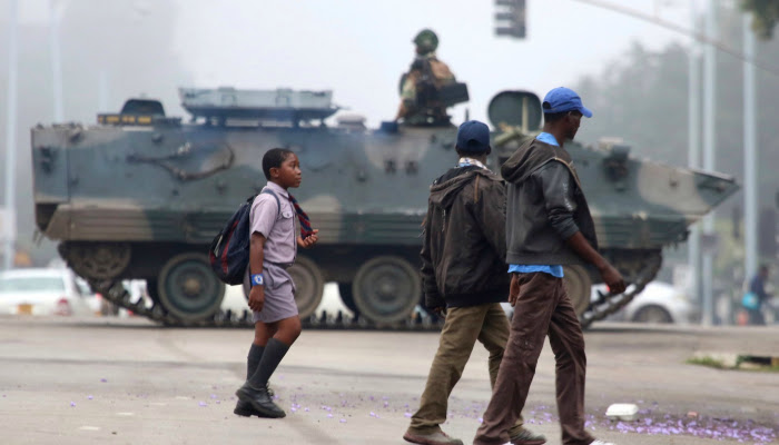 An armored tank is seen blocking part of an intersection as citizens continue about their daily lives and walk past