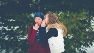 Two girls appear to be gossiping as the girl on the white is whispering into the girl on the left's ear and girl on the left appears to be shocked by what she is hearing