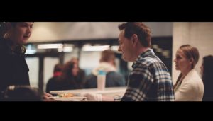 A man in a soup kitchen serves a homeless teen a hot plate of food.