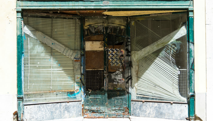 A derelict storefront with falling, dirty blind in the two windows surrounding the dirty, board/paper covered door