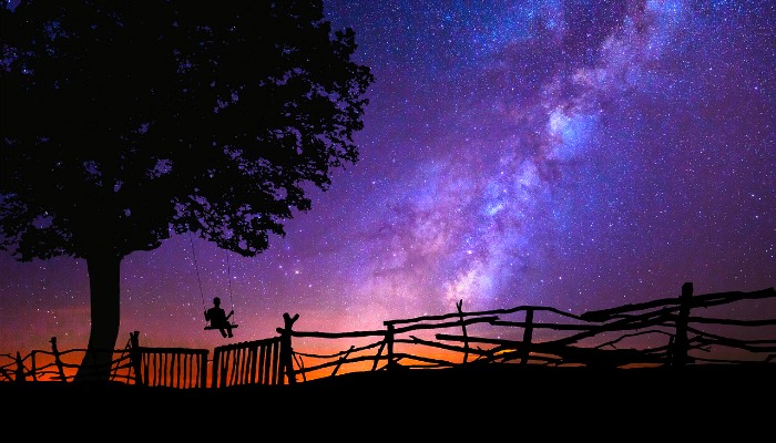 Person on swing looking at night sky and stars.