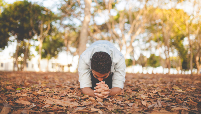 man praying on ground covered with leaves