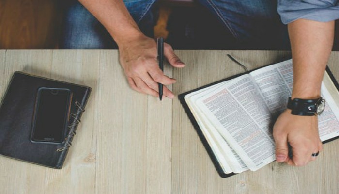 Man's hand with scriptures, cell phone, and journal on a table