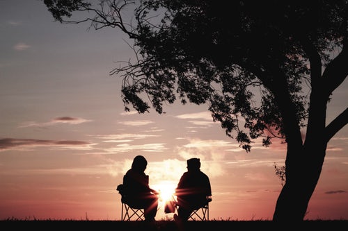 Two people sitting in lawn chairs with a pink sunset as a backdrop