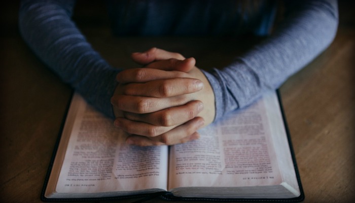 Man folding hands over scriptures