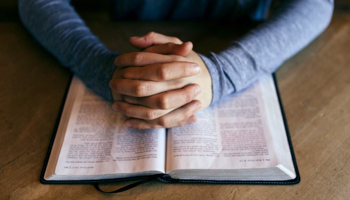 Hands folded over an open Bible.