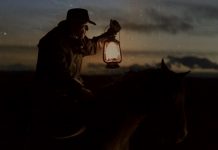 Cowboy riding a horse, holding a lantern.