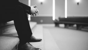 B&W legs of man praying alone in church