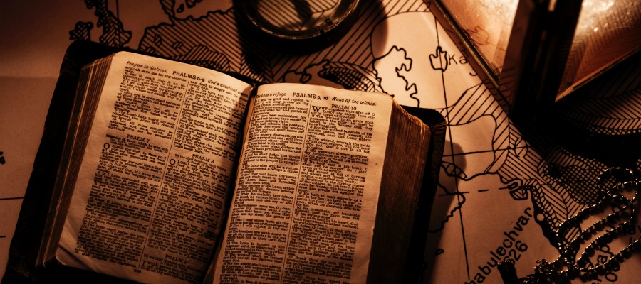 An open bible on top of a map, next to a compass and lantern.