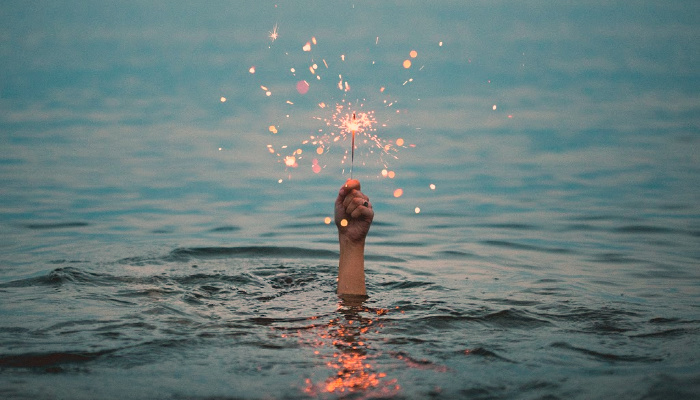 Hand holding sparkler above water.
