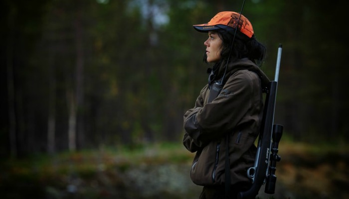 Woman standing in forest with a gun on her back