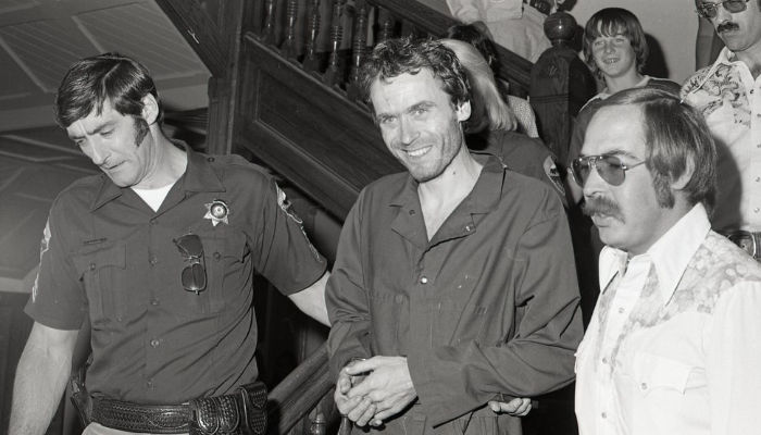 ted bundy being escorted by a police officer