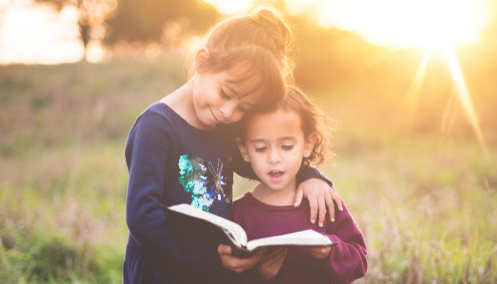 sister siblings hugging and reading scriptures out loud