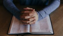 man's praying hands on scriptures