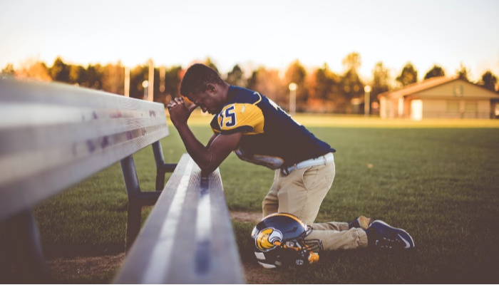 young man football player praying on sideline