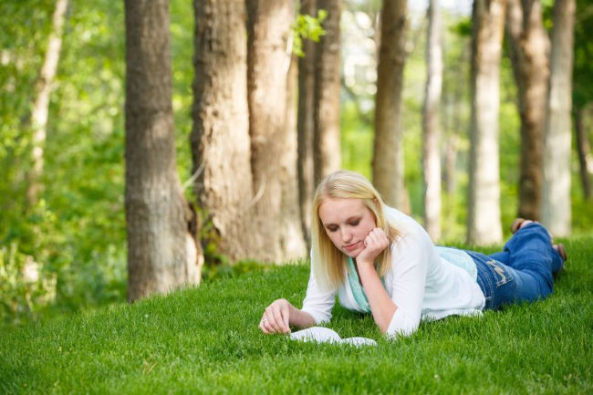 young woman laying on the grass reading the book of mormon