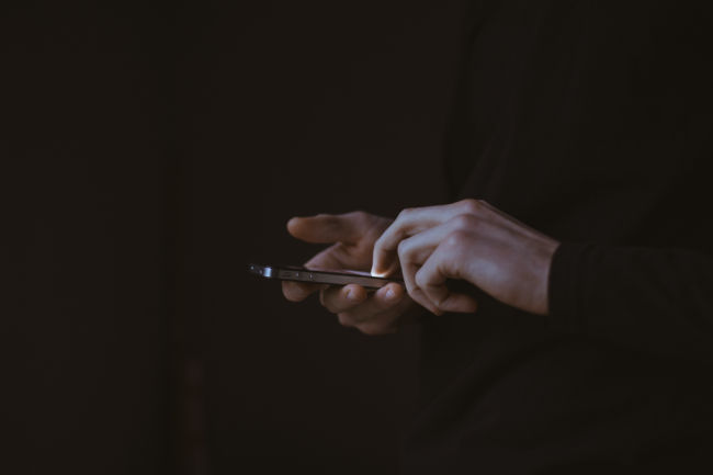 manos sosteniendo un teléfono inteligente en la oscuridad mirando las redes sociales