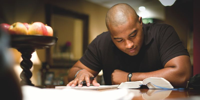 man reading his scriptures at a table