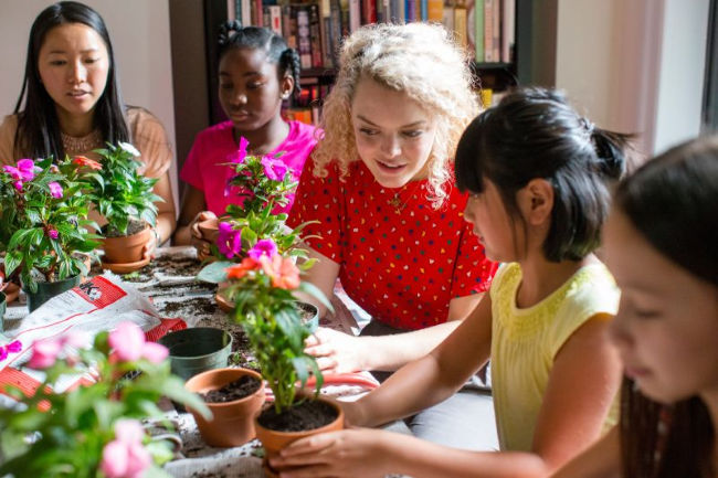 young woman helps girls plant flowers for a church activity